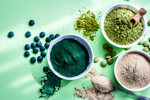 Nutritional supplements: Spirulina, Maca and Moringa powder and pills in white bowls shot from above on abstract green background. High resolution 42Mp studio digital capture taken with Sony A7rII and Sony FE 90mm f2.8 macro G OSS lens