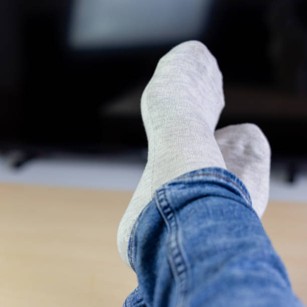 Relaxing woman laying in sofa front of TV, holding her legs on table Relaxing woman laying in sofa front of TV, holding her legs on a table, square format legs crossed at ankle stock pictures, royalty-free photos & images