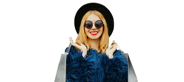 Fashionable portrait of stylish blonde woman with two shopping bags wearing a blue faux fur coat, black round hat on colorful background