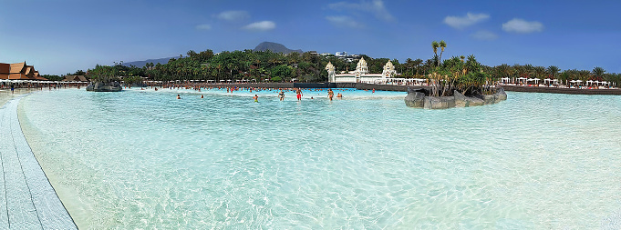 Costa Adeje, Tenerife, Spain - July 16, 2019: People swimming and enjoying artificial wave in popular Siam waterpark at Tenerife island. The Siam is the largest and the most spectacular water attraction in Europe.
