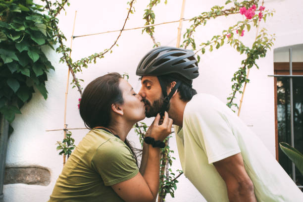 joven pareja enamorada besándose afuera con plantas y flores. chica poniéndose un casco de bicicleta a un niño mientras se besaba. copyspace. - heterosexual couple fotografías e imágenes de stock