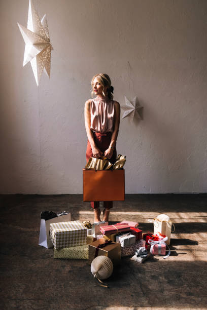 belle femme debout avec de nombreux cadeaux de noël à la maison - women holding shopping bag living room photos et images de collection