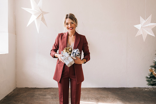 Happy female in red suit holding Christmas gifts in hands at home