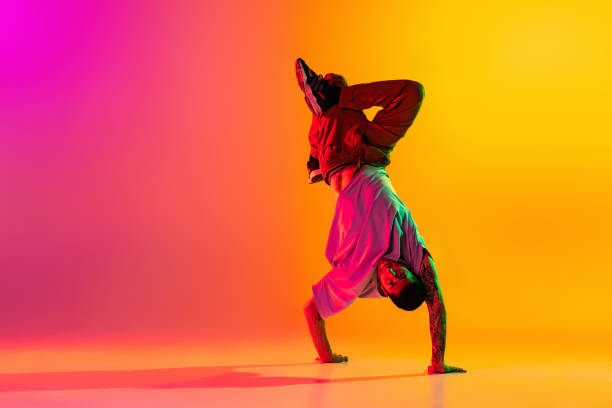 네온 빛의 댄스 홀에서 그라데이션 핑크 옐로우 배경 위에 고립 된 캐주얼 한 옷을 입고 춤을 추는 젊은 세련 된 남자의 초상화. - breaking 뉴스 사진 이미지
