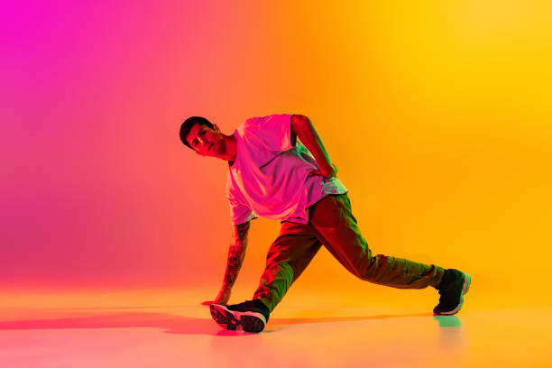 istock Solo performance. Young man, break dancing dancer ptacticing in casual clothes isolated over gradient pink yellow background at dance hall in neon light. 1335873292
