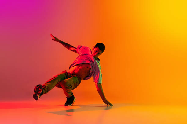 istock Caucasian man, break dancing dancer ptacticing in casual clothes isolated over gradient pink yellow background at dance hall in neon light. 1335873296