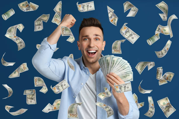 istock Happy young man with dollars under money rain on blue background 1335875806