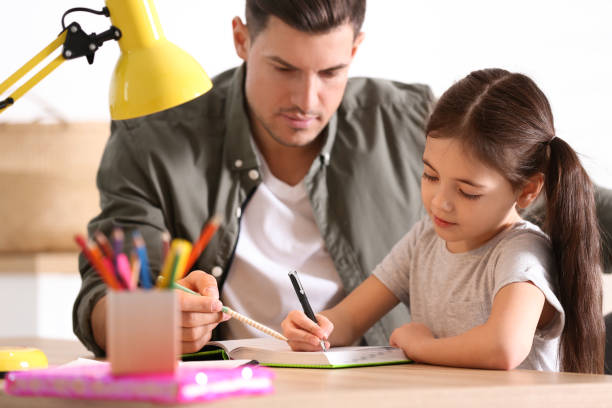 istock Man helping his daughter with homework at table indoors 1335875834