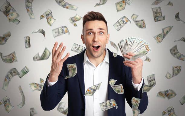 istock Happy young man with dollars under money rain on light background 1335875847
