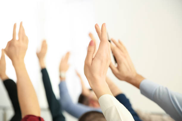 istock People raising hands to ask questions at business training on light background, closeup 1335876621