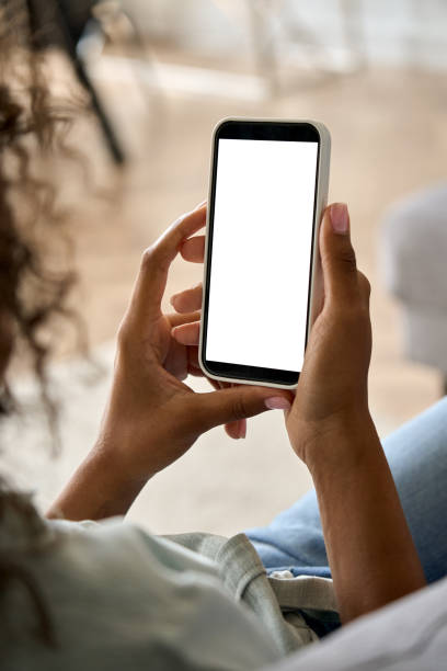 African American woman hand holding phone with mockup white blank display. Young African American woman hands holding cell phone with mockup white blank display, empty screen for app ads at home. Mobile applications technology concept, over shoulder close up view. looking at cell phone screen stock pictures, royalty-free photos & images