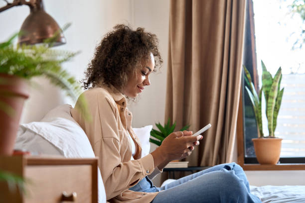 istock Young happy African American woman using cellphone sitting on bed. 1335876757