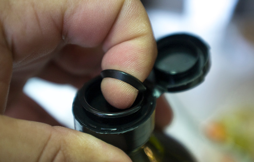 Finger opening a sealed olive oil bottle with an inner pull-off plastic tab underneath the cap. Closeup