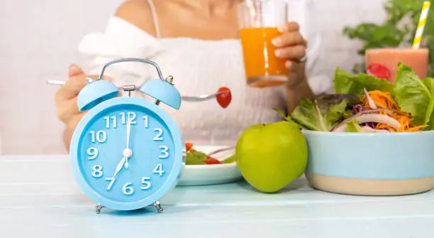 Close up of blue clock it timer for  woman restricted eating. Healthy foods between clock hands, daily eating window, fasting period, weight loss concept