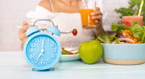 close up of blue clock it timer for  woman restricted eating. healthy foods between clock hands, daily eating window, fasting period, weight loss concept - weight apple loss weightloss imagens e fotografias de stock