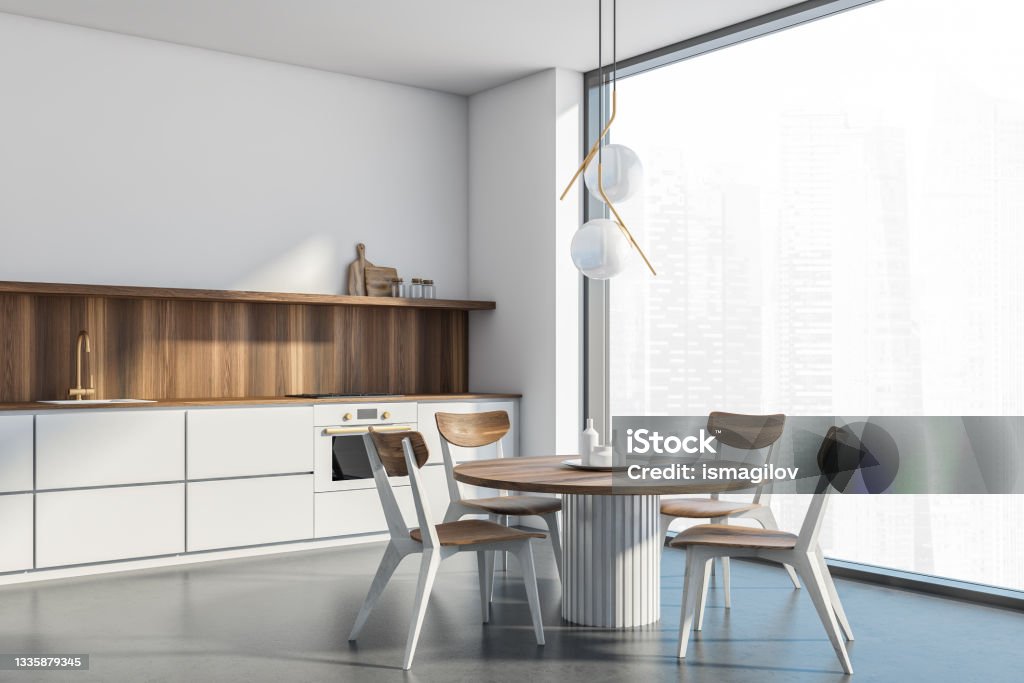 White kitchen room corner with panoramic view, wooden furniture Corner of the interior with the white panoramic kitchen area. Wooden table, chairs and splashback of the cabinet. Original chandelier, white walls and concrete flooring. 3d rendering Dining Table Stock Photo