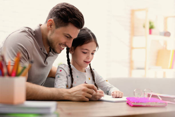 istock Man helping his daughter with homework at table indoors 1335879422
