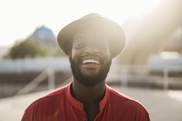 Young african man smiling on camera outdoors with city in background - Main focus on nose