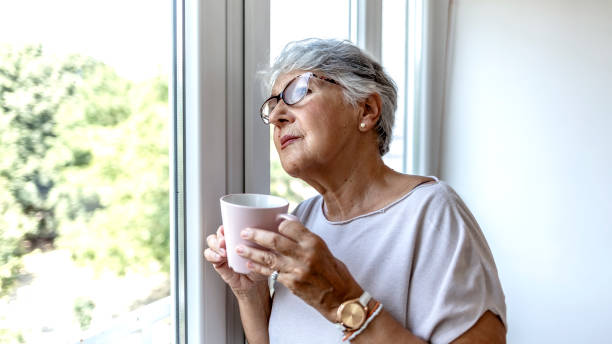 istock Depressed lonely lady standing alone and looking through the window. 1335881237