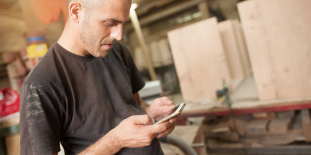 istock Carpenter artisan resting in workshop and scrolling on smartphone 1335882098