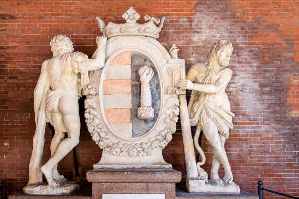 Two Hercules hold the coat of arms of Cremona: the sculpture is located under the portico of the Loggia dei Militi, an historical building built in 1292