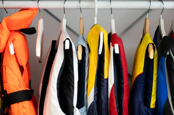 Life jackets and life west for both kids and adults hanging on the rack indoors.