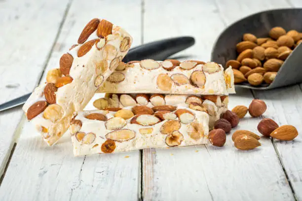 Turron blocks with almonds and hazelnuts on rustic wooden table with knife and shovel