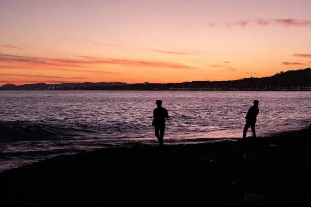 A colored image of the sunset from the beach at Nice, France towards the sea, two people are seen at the beach as silhouettes.
