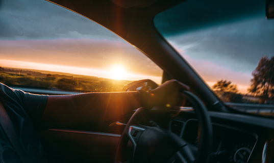 man is driving on the road under the sunset, one hand holding the steering wheel