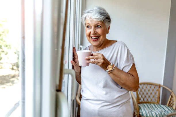 istock A senior Caucasian woman leans against a window frame while looking outside thoughtfully. 1335890157