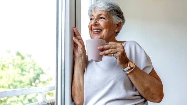 istock A senior Caucasian woman leans against a window frame while looking outside thoughtfully. 1335890177