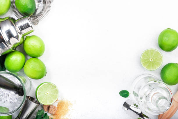 istock Mojito cocktail making. Mint, lime, ice, white rum, cane sugar - ingredients and bar utensils. Top view, white background. Flat lay 1335890317