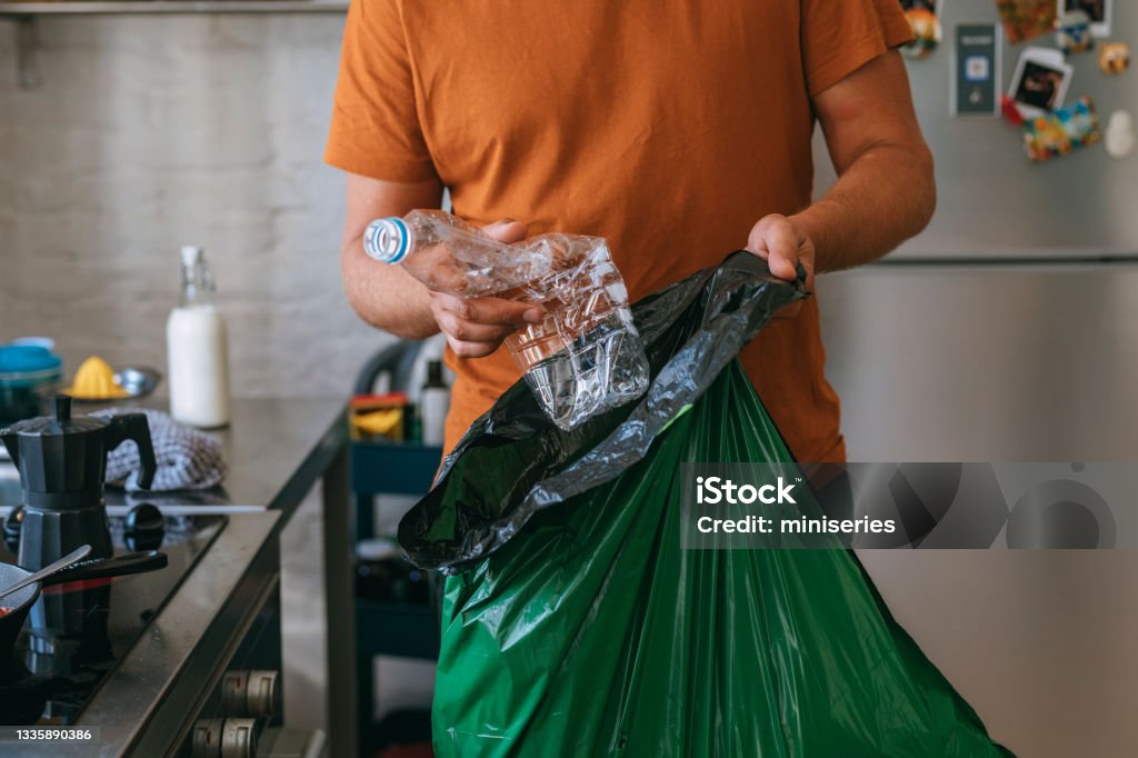Cooking At Home: Handsome Man With Garbage Bag Handsome young man holding green garbage bag and plastic bottle Recycling Stock Photo