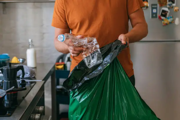 Handsome young man holding green garbage bag and plastic bottle