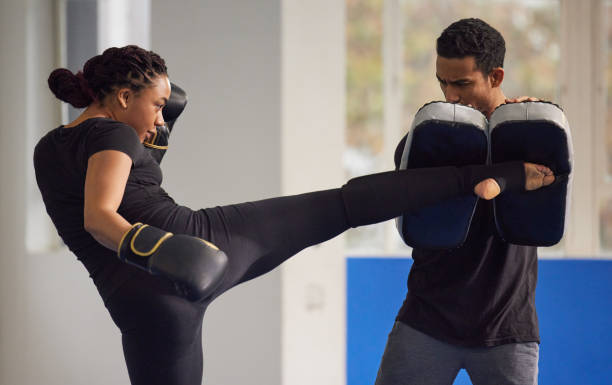 ujęcie młodej kobiety ćwiczącej kickboxing ze swoim trenerem na siłowni - kickboxing zdjęcia i obrazy z banku zdjęć