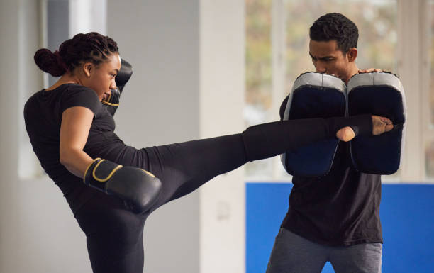 tiro de uma jovem praticando kickboxing com seu treinador em uma academia - kickboxing muay thai exercising sport - fotografias e filmes do acervo