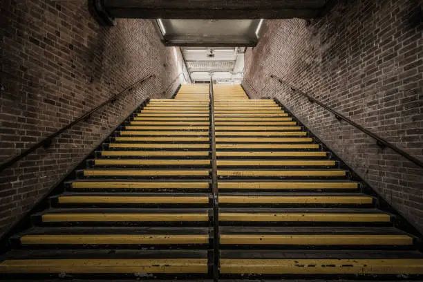 Large stairs with yellow strips, going up to the tube station, two large brick walls on the sides.