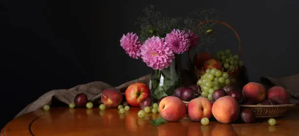 Photo of Panorama with fruits and a bouquet of summer flowers on a dark background