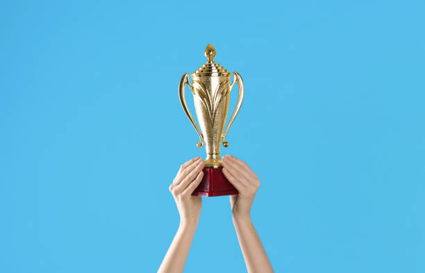 istock Woman holding gold trophy cup on light blue background, closeup 1335895215