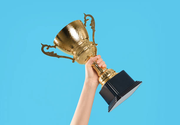 Woman holding gold trophy cup on light blue background, closeup Woman holding gold trophy cup on light blue background, closeup trophy award stock pictures, royalty-free photos & images