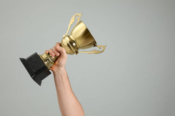 istock Man holding gold trophy cup on light grey background, closeup. Space for text 1335895249