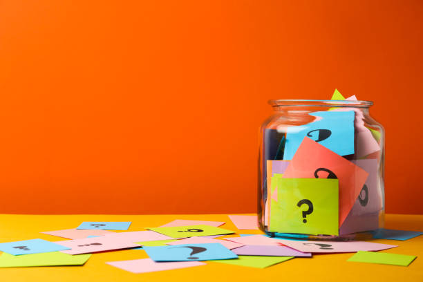 tarjetas de colores con signos de interrogación en frasco de vidrio sobre fondo naranja. espacio para texto - question fotografías e imágenes de stock