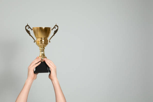 istock Man holding gold trophy cup on light grey background, closeup. Space for text 1335895294