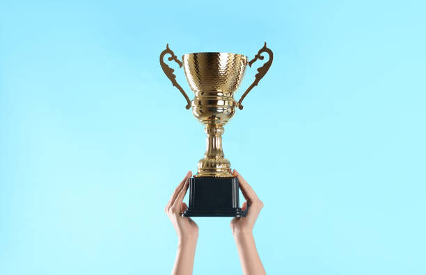 istock Woman holding gold trophy cup on light blue background, closeup 1335895367
