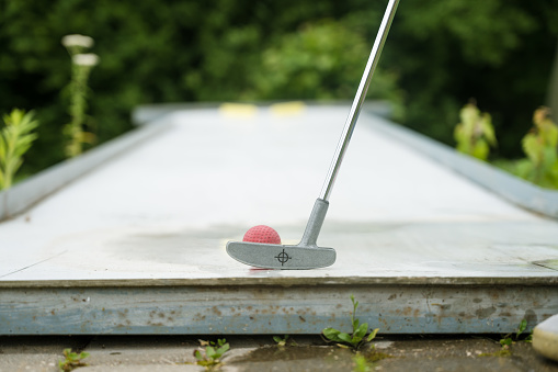 Close-up of playing mini golf. Red ball and stick. Summer outdoor game.