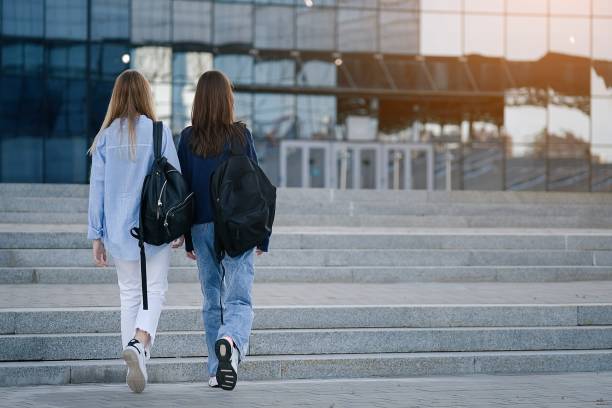 вид сзади двух студентов, идущих и разговаривающих в университетском городке - university education walking teenage girls стоковые фото и изображения