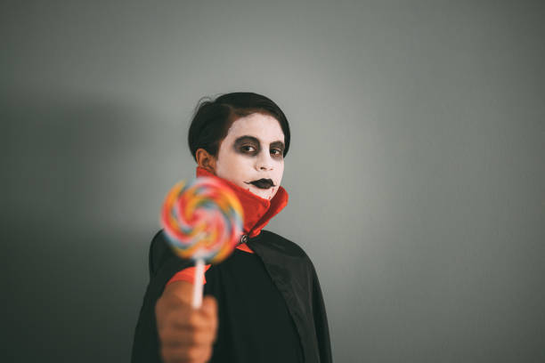 Girl with Dracula make-up plays with a lollipop alluding to the candies and sweets given out on halloween