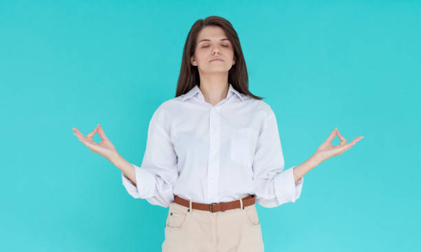 istock Beauiful young female makes mudra sign, relaxes after hard working day, keeps eyes shut, practises yoga against blue background. Young pretty woman meditates indoor. Relaxation concept 1335900929