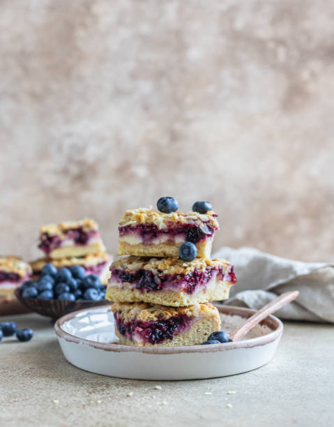 Crumble cheesecake bars with blueberry filling and fresh blueberries, concrete background. Bar slices with cheesecake, blueberry and streusel. Crumble cheesecake bars with blueberry filling and fresh blueberries, concrete background. Bar slices with cheesecake, blueberry and streusel. Selective focus. cobbler dessert stock pictures, royalty-free photos & images