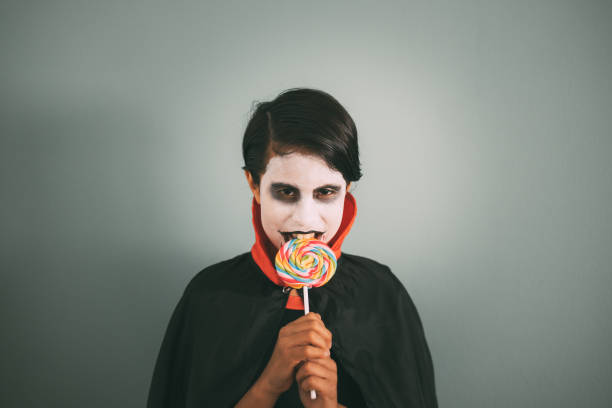 Girl in Dracula costume bites a lollipop while looking at the camera